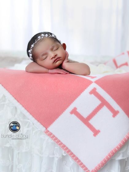 This newborn girl rests her chin on her hands, sleeping on a personalized pink and white blanket, showcasing how I can incorporate custom items into a session.