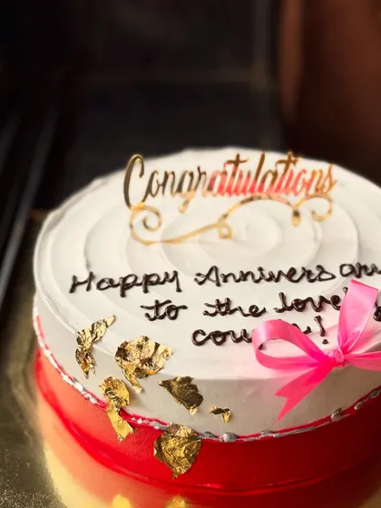 A simple and elegant anniversary cake with a "Congratulations" topper and gold leaf details.