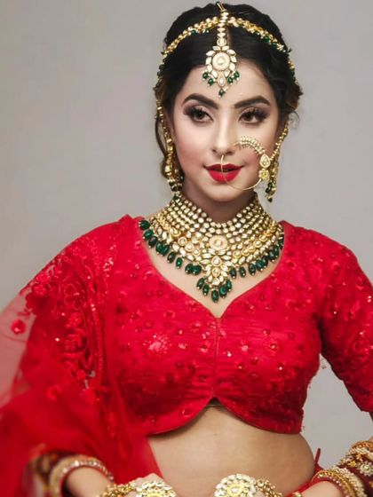 A classic red-and-green bridal combination. The model wears a red lehenga with a Pachi Kundan necklace featuring emerald green drops.
