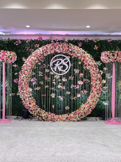 This engagement stage is a vision in pink and green. A large circular floral arrangement serves as the centerpiece, set against a lush green hedge wall for a fresh, garden-like feel.