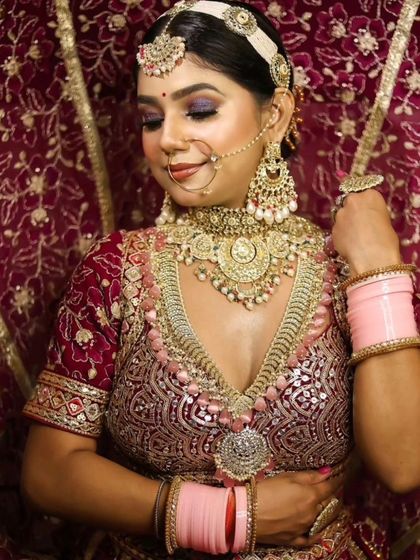 A bride wearing a heavy, layered jewellery set with pink accents, perfectly complementing her maroon and pink lehenga.