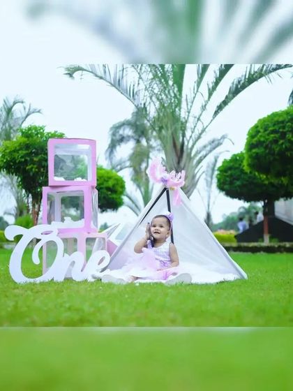 This wide shot shows the full outdoor setup, featuring a teepee tent and a large 'One' sign, perfect for a first birthday photoshoot in a park.