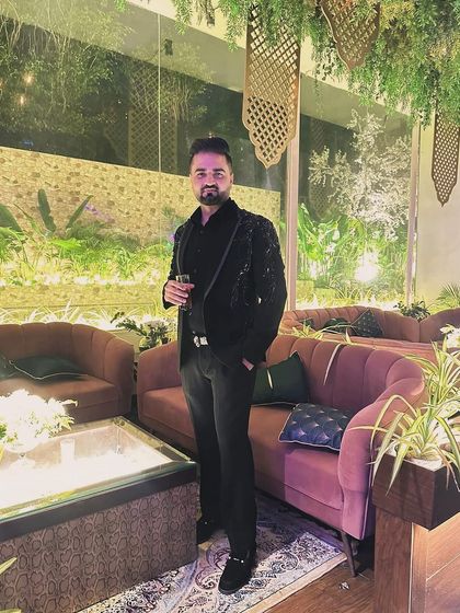 A client looking sharp at an evening event. He is wearing a black tuxedo with intricate tonal embroidery, showcasing a look of understated, confident luxury.