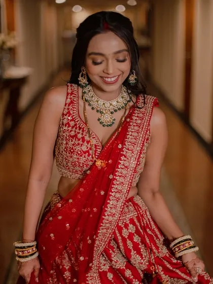 A joyful bridal portrait, capturing a beautiful, natural smile. The focus is on the bride's happiness and the exquisite details of her red lehenga.