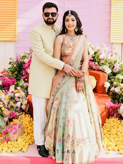 The couple posing for a portrait at their vibrant and floral-heavy Haldi, a perfect picture of love and happiness.