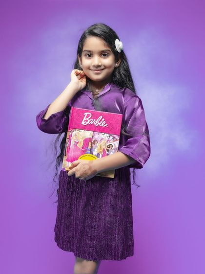 Celebrating her seventh birthday with her favorite Barbie book. This personal touch makes the portrait unique to her. The simple purple background complements her dress and keeps the focus on her happy, gentle smile.