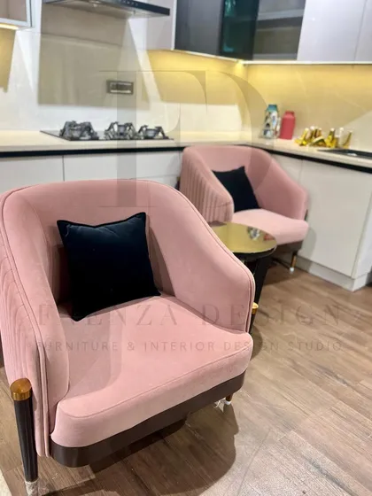 A pair of blush-pink armchairs with pleated backs and tapered legs with brass caps. These chairs are perfect for adding a touch of soft, modern glamour to a living room or kitchen seating area.
