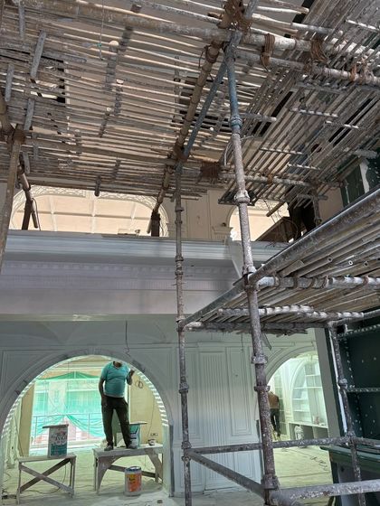 Workers on scaffolding apply finishes to the high walls and arched windows of a double-height space. This labor-intensive process is essential for achieving the polished look of a classical interior.