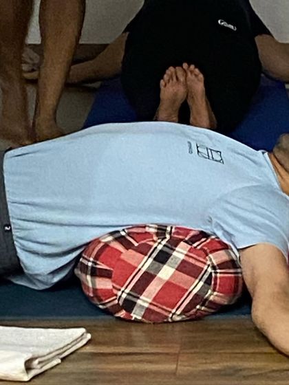 A close-up of a student in Matsyasana (Fish Pose) supported by a bolster. This opens the throat and chest, stimulating the thyroid gland.