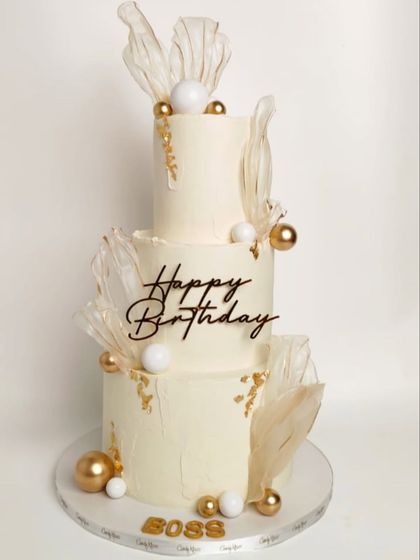A special three-tiered cake for a "Boss," created on short notice. This elegant white and gold design features abstract sails and metallic spheres.