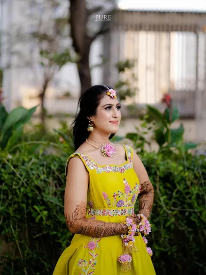 A beautiful outdoor portrait of the bride on her Mehndi day. Her yellow dress and floral jewelry look stunning against the lush green background.