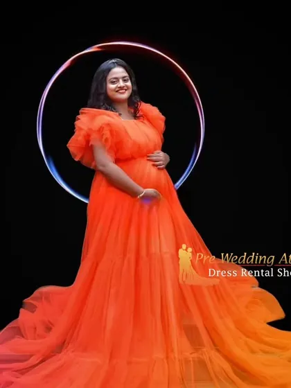 This bright orange ruffled gown is perfect for a modern and vibrant studio maternity shoot. The voluminous tulle skirt and ruffled shoulders create a high-fashion look against a simple black background.