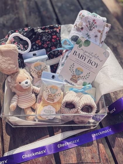 A different view of the baby boy arrival hamper, showing the soft clothing and other essentials neatly arranged. The clear box and custom ribbon add a touch of modern luxury.