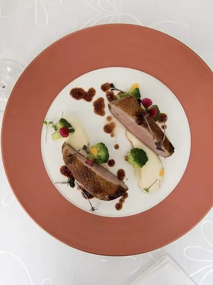 An overhead shot of our pan-seared duck breast, elegantly plated with a rich sauce and fresh garnishes.