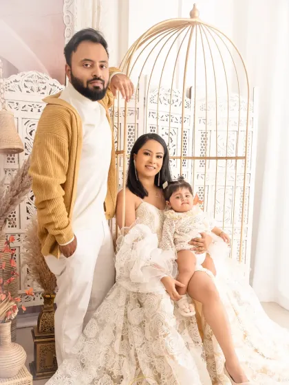 A stylish family portrait featuring a mother, father, and their baby girl in a chic, neutral-toned studio setting.