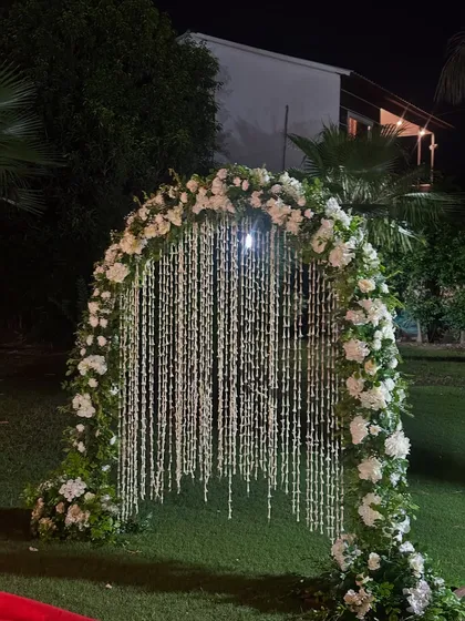 A close-up of a beautiful floral entrance arch. This design features a cascade of white flower strings (rajanigandha) hanging within a frame of lush white roses and greenery, creating a fragrant and picturesque welcome for guests.