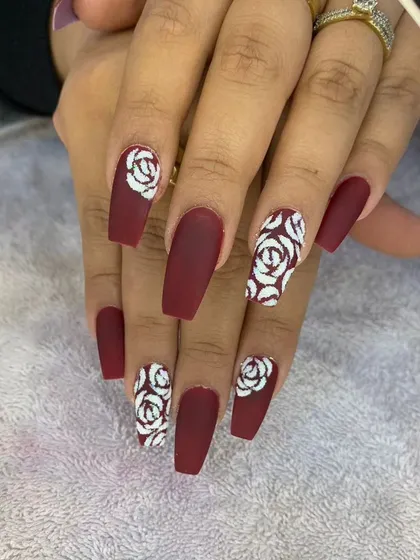 A bold and stylish set featuring matte burgundy nails with white Chanel-inspired rose accent nails. This design is perfect for a chic and high-fashion look.