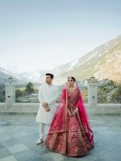 A stylish, full-length portrait of the couple on a terrace overlooking the mountains, showcasing their elegant wedding attire.