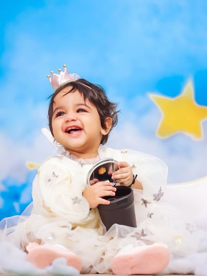 A close-up of a happy baby girl enjoying her celestial-themed photoshoot. Her bright smile and the whimsical starry backdrop make for a magical combination.