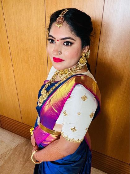 A side profile showcasing the elegant hair bun, temple jewelry, and flawless makeup. The contrast between the blue saree and the white embroidered blouse is just beautiful.