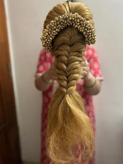 A fishtail braid paired with a golden floral accessory, created on a mannequin head. This is a great example of how we practice combining traditional and modern elements in my hair education classes.