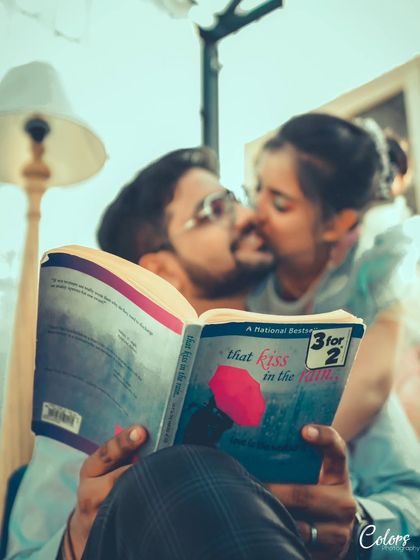 A creative and intimate shot where the couple kisses behind a book titled "That Kiss in the Rain," telling a story within a photo.