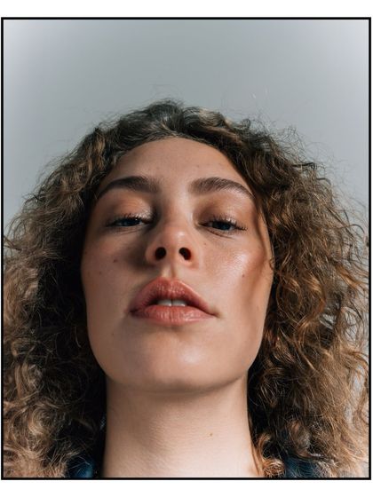 An intense, low-angle close-up portrait for Flanelle Magazine, focusing on the model's direct and confident gaze.