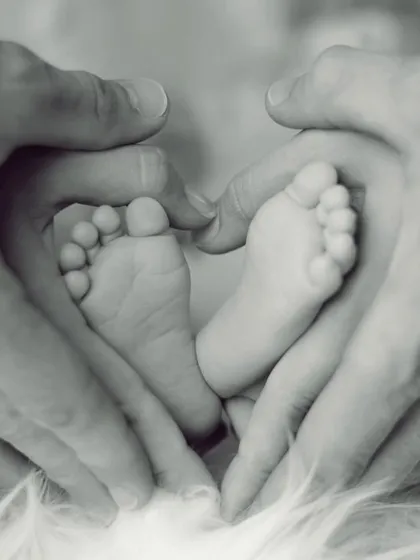 A classic and heartwarming newborn detail shot. Parents' hands form a heart shape around their baby's tiny feet, symbolizing the love and protection surrounding their new arrival.