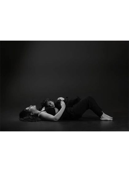 A mother lies on the floor with her daughter resting peacefully on her chest. This unconventional pose, captured in dramatic black and white, speaks volumes about trust and comfort.