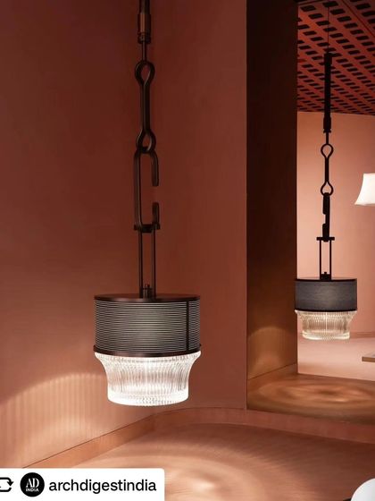 This industrial pendant light is showcased in a corner, allowing its unique form and the quality of its light to be the main focus. The reflection in the background hints at the depth of the space.