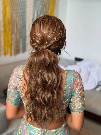 A chic and modern messy ponytail. This hairstyle is elevated with delicate pearl accents scattered throughout, making it perfect for a sangeet or reception.