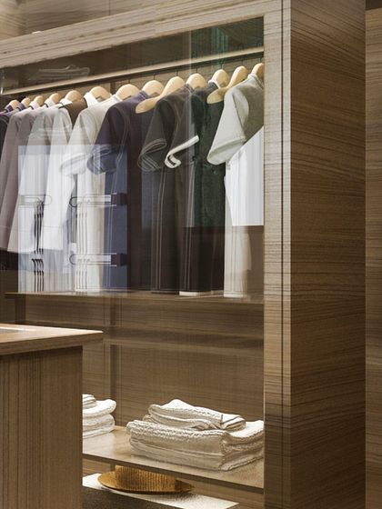 This view highlights the glass-fronted section of a wood veneer wardrobe, allowing for a quick view of suits and shirts while protecting them from dust.