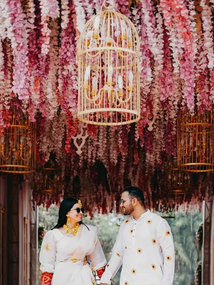 A stunning portrait of the Haldi couple under a ceiling of pink and purple flowers. The grand decor and their joyful expressions perfectly capture the festive atmosphere.