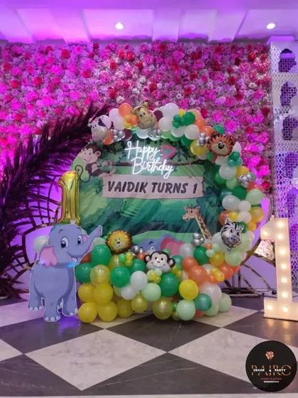 The jungle-themed first birthday stage for Vaidik. This image shows the complete setup, including the circular backdrop, animal cutouts, and light-up "1" prop.