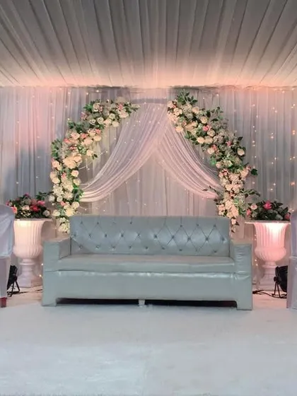 An all-white theme brings a timeless elegance to any event. This reception stage features a beautiful floral arch, soft drapery, and decorative white trees, all illuminated to create a dreamy and sophisticated setting.