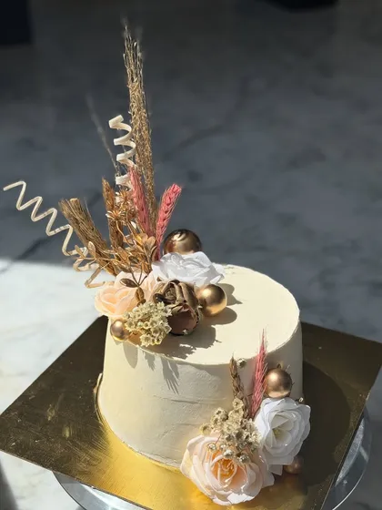 A chic and modern cake decorated with dried botanicals, gold spheres, and delicate white flowers. This design is perfect for a rustic or boho-themed celebration.