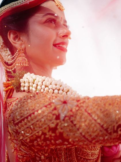 A radiant, happy shot of bride Supriya during her ceremony. The focus is on the heavily crafted sleeve of her red blouse, featuring zari, zardosi, and sequin embroidery.