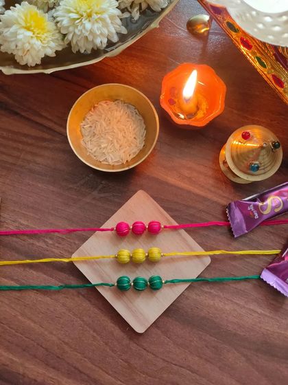 A set of colorful thread-bead rakhis. These are available in bright pink, yellow, and green, perfect for a festive celebration.
