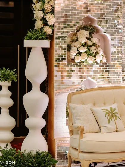 A detail shot of the lounge at the "Enchanted Forest" wedding, where a classic sofa is placed next to modern white totem vases against a mirrored brick wall.