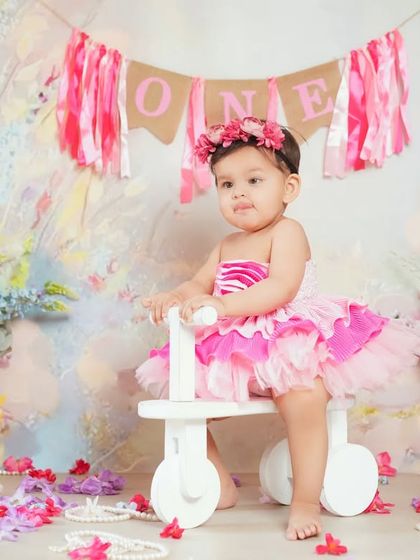 A first birthday portrait with a floral theme. The 'ONE' banner and little tricycle add a celebratory touch.