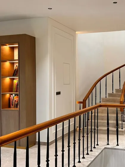 A custom-built, back-lit library cabinet we crafted for a project by Aura Designgram. The warm wood and integrated lighting create an inviting feature along the elegant staircase.