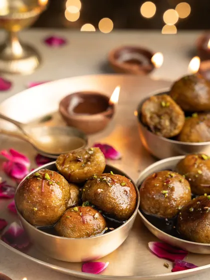 A festive shot of gulab jamun made with jaggery, set against a backdrop of diyas. The warm, moody lighting enhances the rich, syrupy texture of this classic Indian dessert.