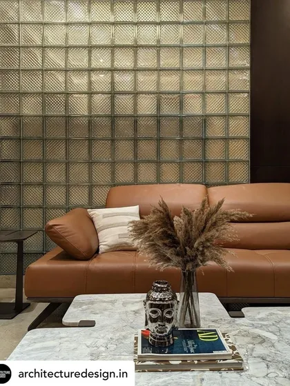 A tan leather sofa is positioned against a textured glass block wall, creating a sophisticated interplay of materials in the family lounge. The space is accessorized with natural elements for a relaxed feel.