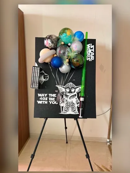 "May the 40s be with you." This creative Star Wars themed display for a 40th birthday features a custom easel with Yoda artwork, a lightsaber, and a unique balloon arrangement that looks like planets from a galaxy far, far away.