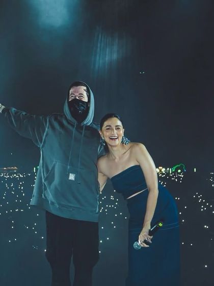 Alan Walker and Alia Bhatt pose for a photo on stage, with a sea of phone lights from the audience behind them.