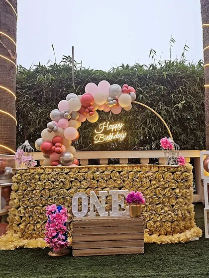 This first birthday setup is all about golden glamour. We designed this stunning outdoor party featuring a table covered in golden roses, a custom balloon arch, a "Happy Birthday" neon sign, and personalized "ONE" photo blocks to celebrate the milestone.