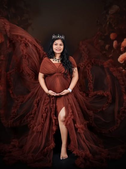 A dramatic and powerful portrait with a "flying gown" effect. The mom-to-be stands like a queen, her gown's train creating wings of fabric behind her.