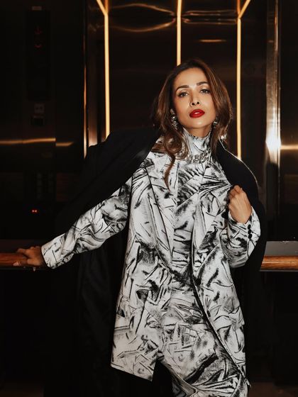 Malaika Arora inside an elevator, a setting that provides a dramatic, moody backdrop with its dark tones and vertical light strips.