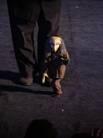 A mysterious, masked marionette character from 'Il Fil'armonico' walks towards the audience, creating a moment of intrigue.