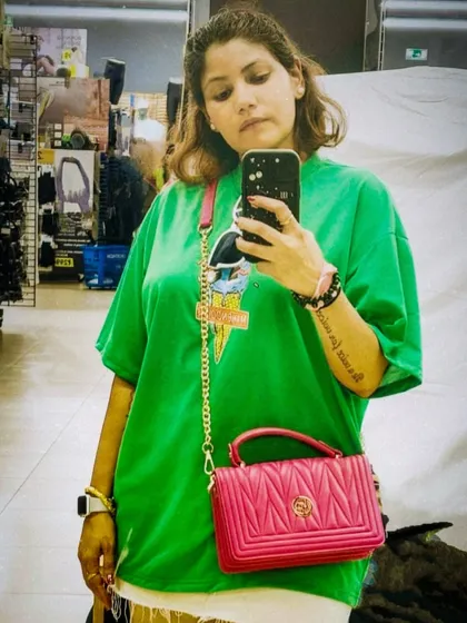 A mirror selfie in a bright green oversized tee and a pink bag, showcasing a bold and casual color combination.